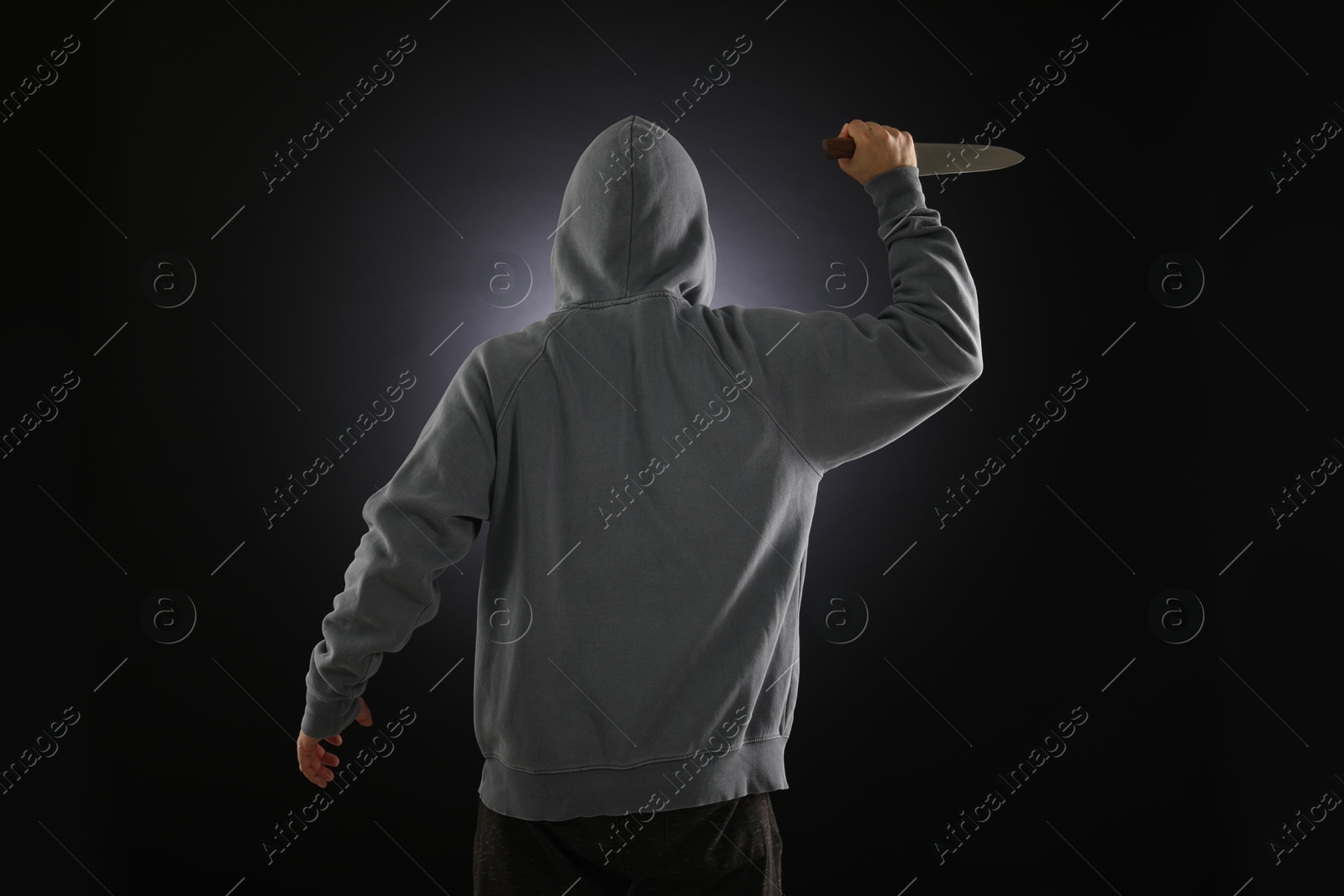 Criminal with knife on dark background, back view Photo of Criminal with knife on dark background, back view