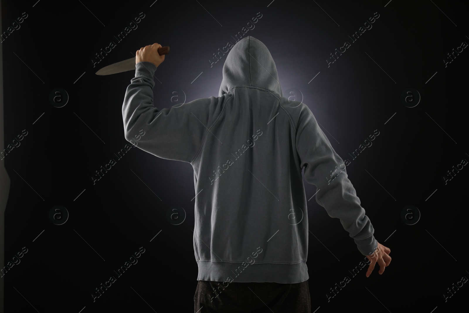 Criminal with knife on dark background, back view Photo of Criminal with knife on dark background, back view
