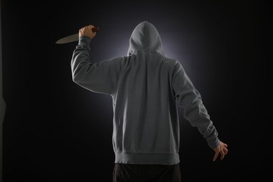 Photo of Criminal with knife on dark background, back view
