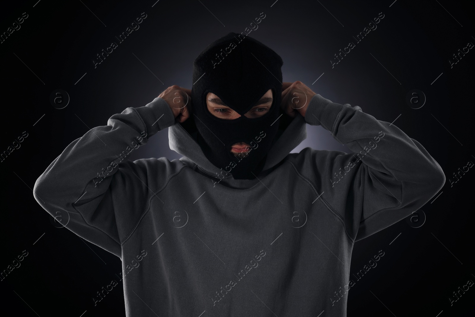 Criminal in mask and hood on dark background Photo of Criminal in mask and hood on dark background