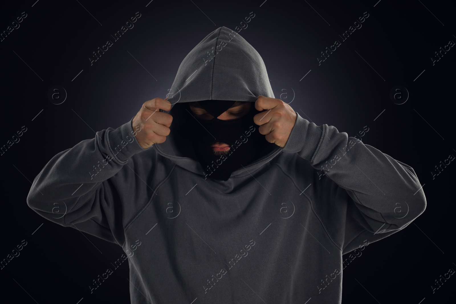 Criminal in mask and hood on dark background Photo of Criminal in mask and hood on dark background