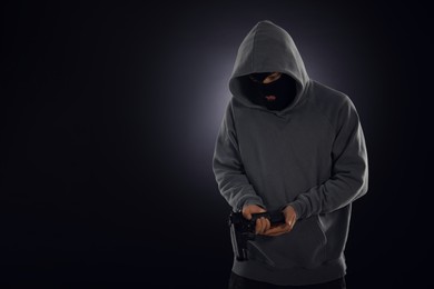 Photo of Criminal in mask with gun on dark background. Space for text