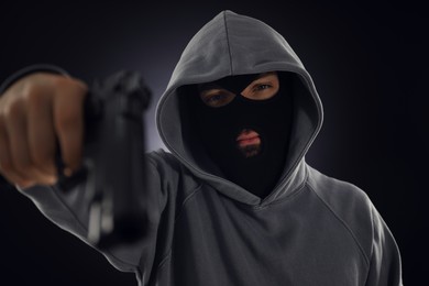 Photo of Criminal in mask with gun on dark background, selective focus