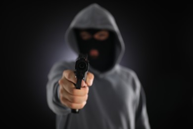Photo of Criminal in mask with gun on dark background, selective focus