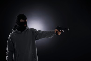 Photo of Criminal in mask with gun on dark background. Space for text