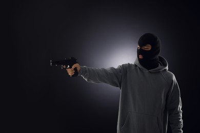 Photo of Criminal in mask with gun on dark background. Space for text