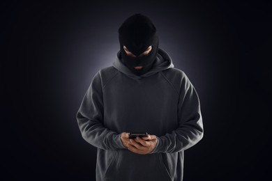 Photo of Criminal in mask with phone against dark background