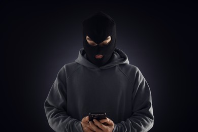 Photo of Criminal in mask with phone against dark background