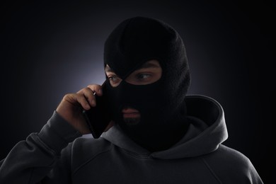 Photo of Criminal in mask talking on phone against dark background