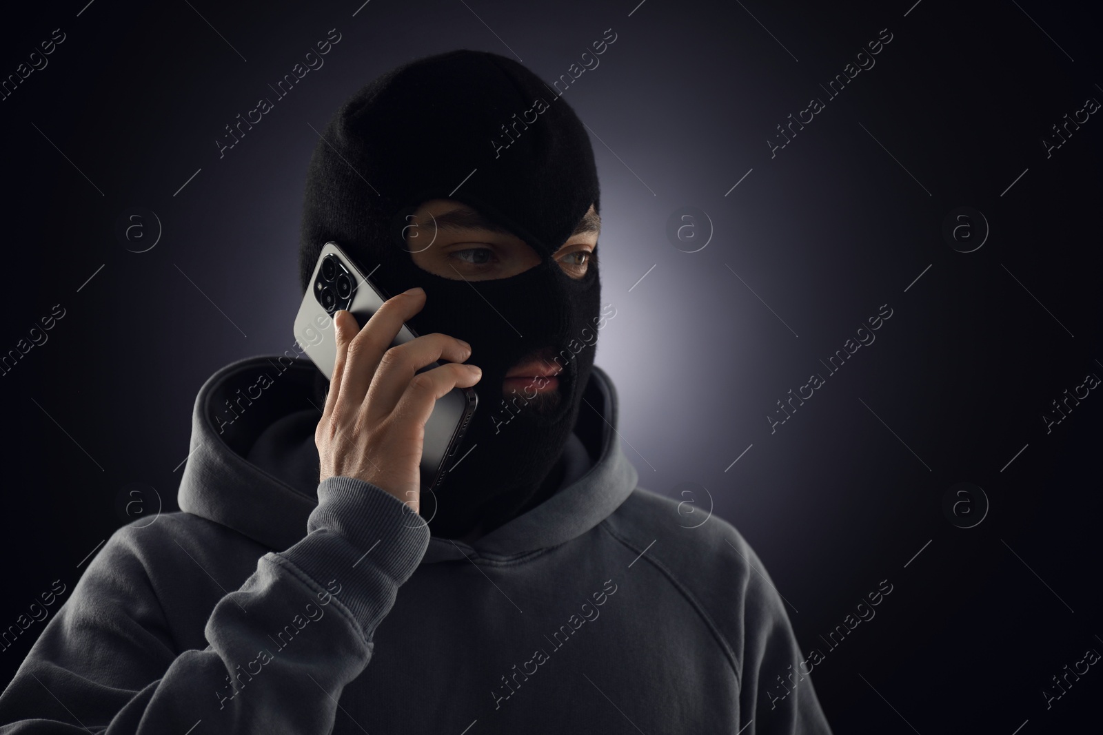 Criminal in mask talking on phone against dark background. Space for text Photo of Criminal in mask talking on phone against dark background. Space for text