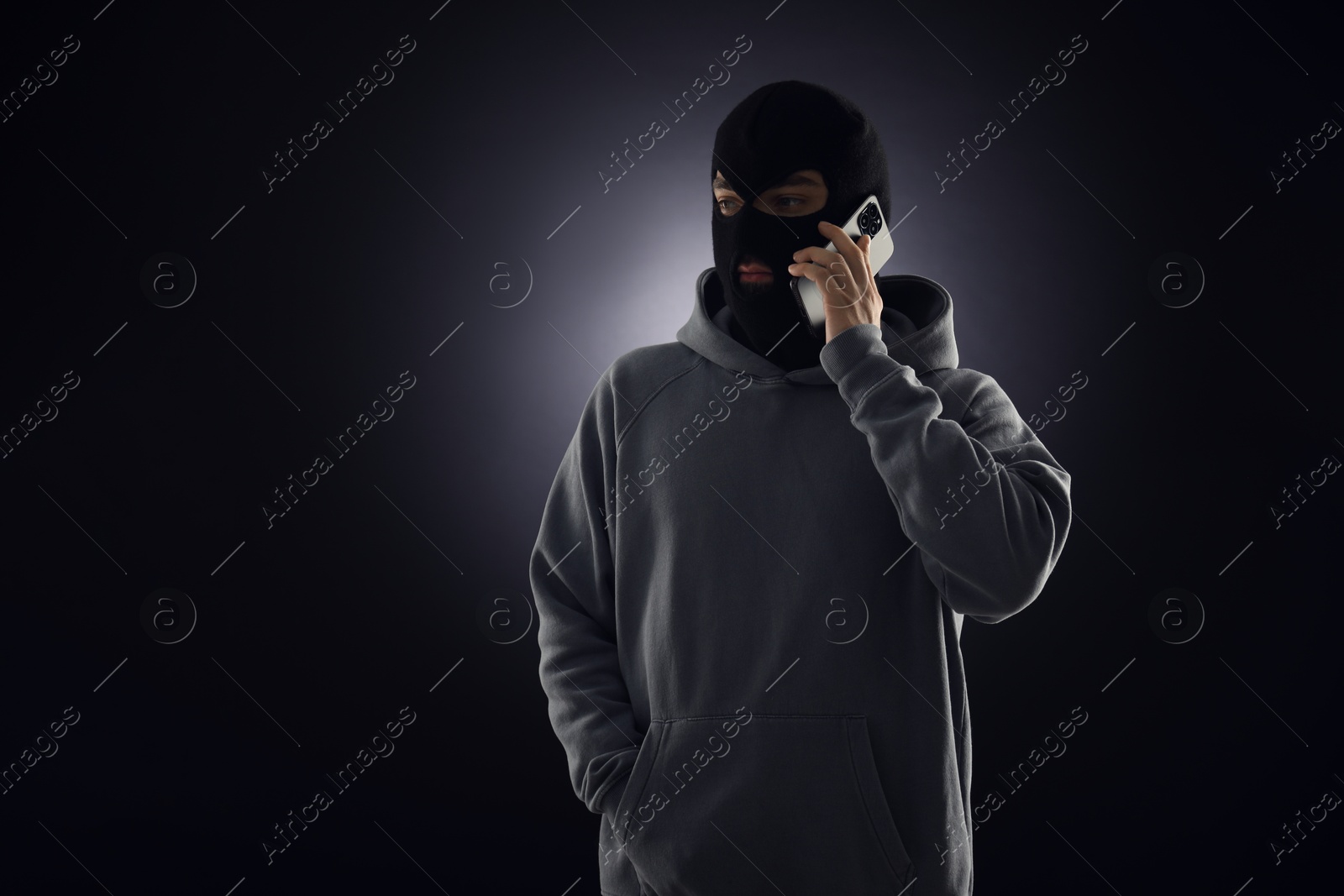 Criminal in mask talking on phone against dark background. Space for text Photo of Criminal in mask talking on phone against dark background. Space for text