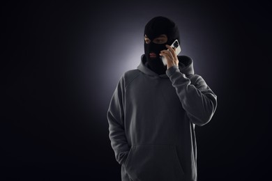 Photo of Criminal in mask talking on phone against dark background. Space for text