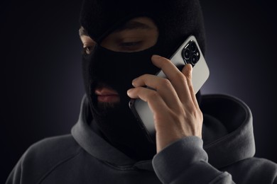 Photo of Criminal in mask talking on phone against dark background