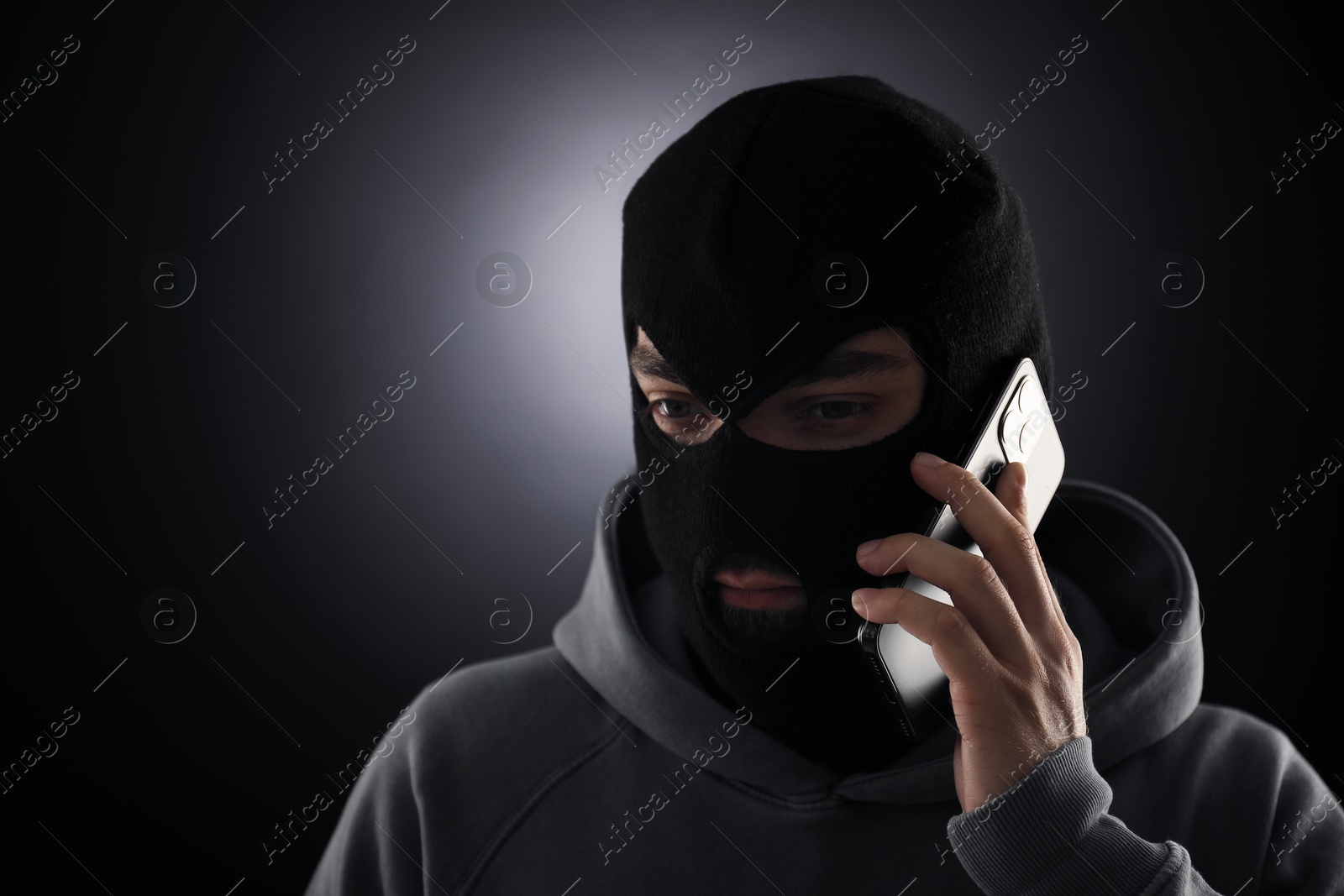 Criminal in mask talking on phone against dark background. Space for text Photo of Criminal in mask talking on phone against dark background. Space for text