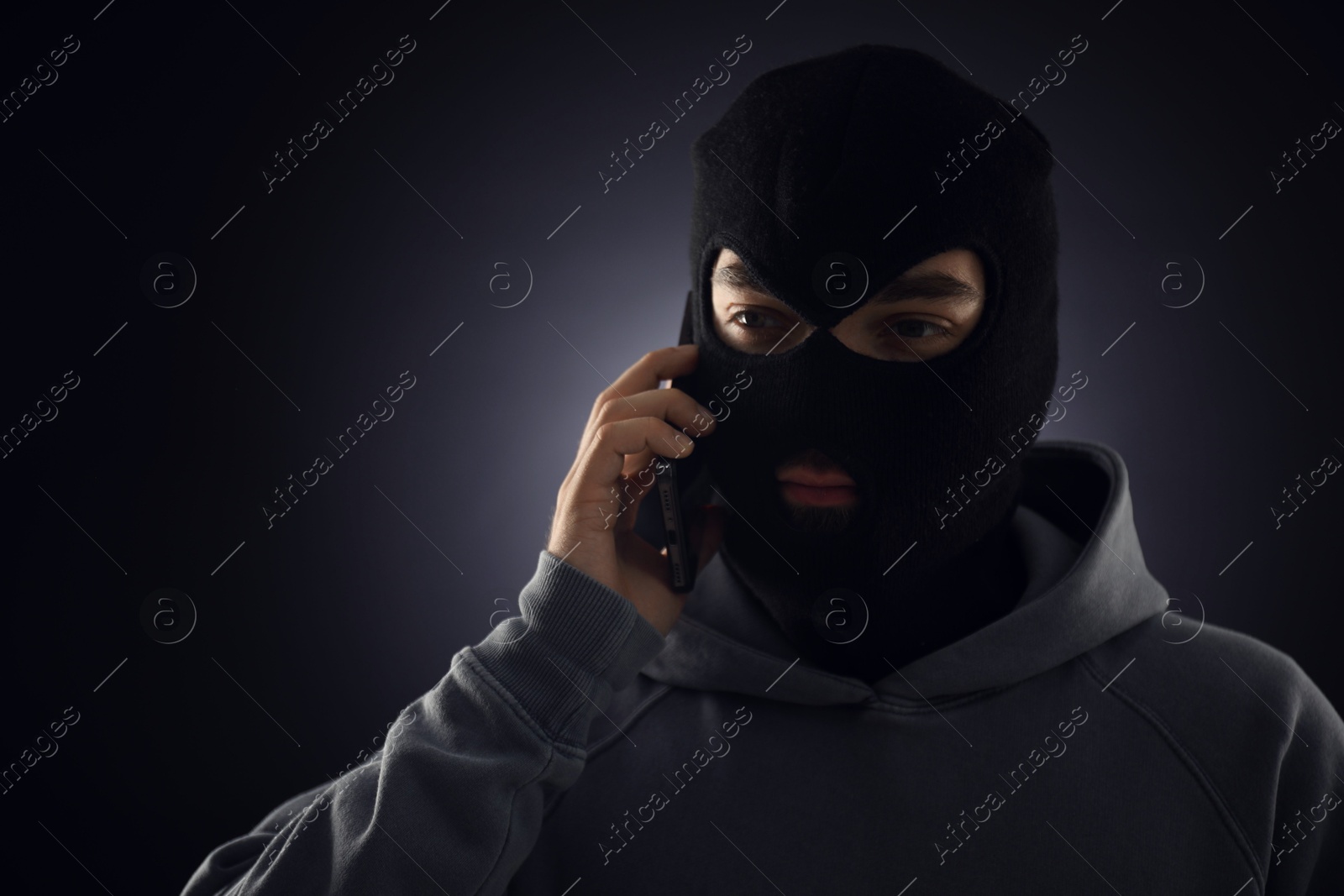 Criminal in mask talking on phone against dark background. Space for text Photo of Criminal in mask talking on phone against dark background. Space for text