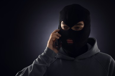 Photo of Criminal in mask talking on phone against dark background. Space for text