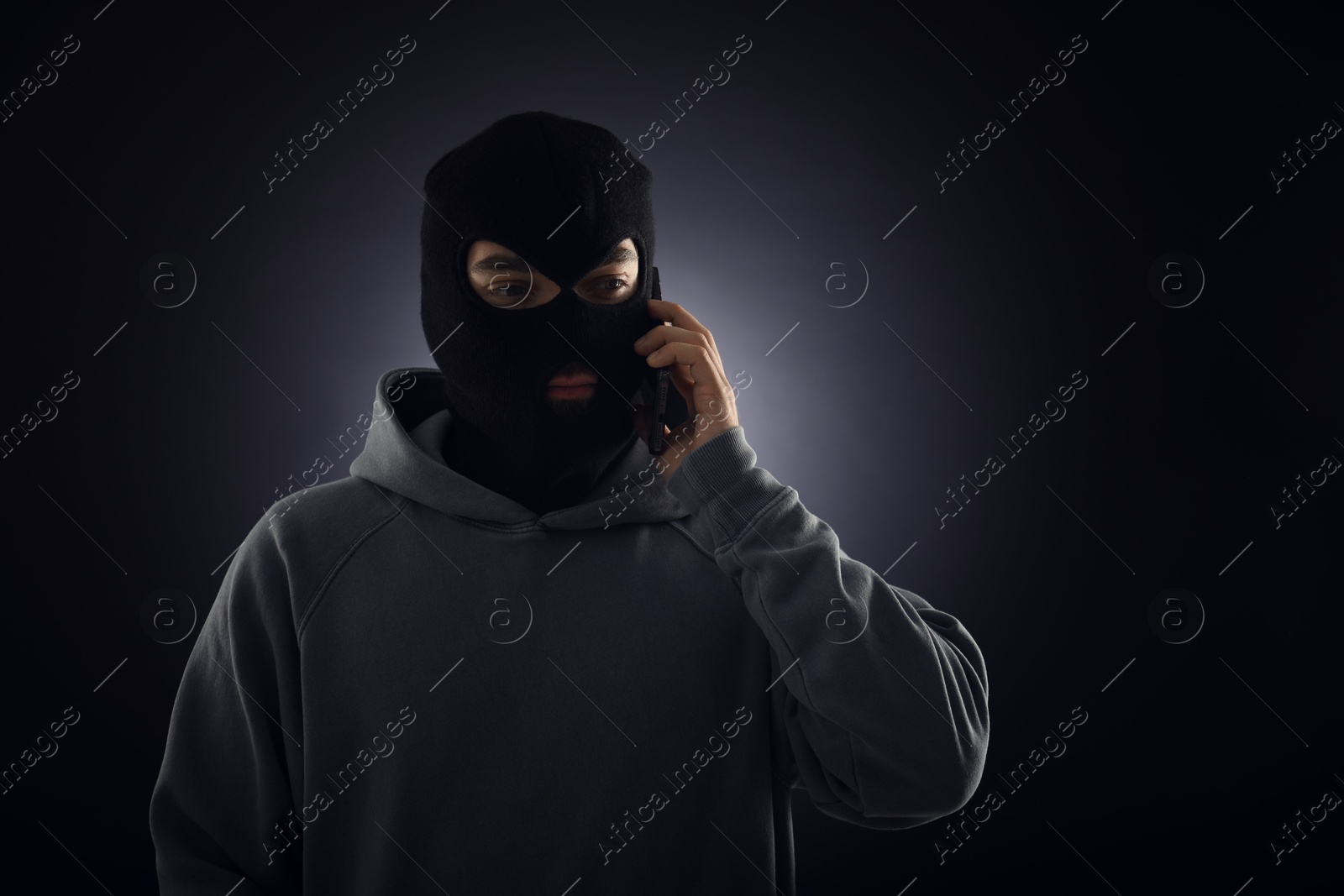 Criminal in mask talking on phone against dark background. Space for text Photo of Criminal in mask talking on phone against dark background. Space for text