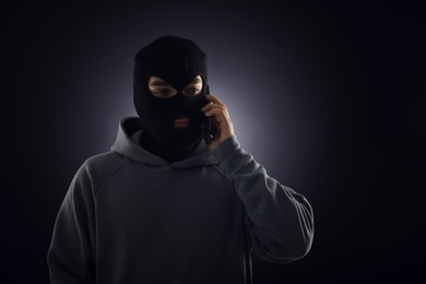 Photo of Criminal in mask talking on phone against dark background. Space for text
