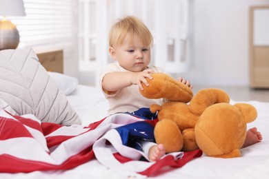 Photo of Cute little child with flag of USA and toy bear on bed at home