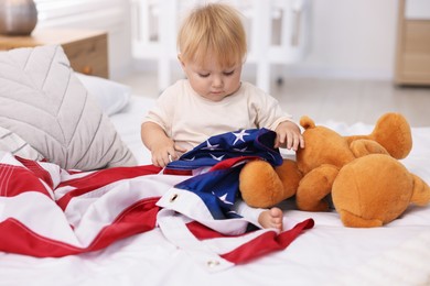 Photo of Cute little child with flag of USA and toy bear on bed at home