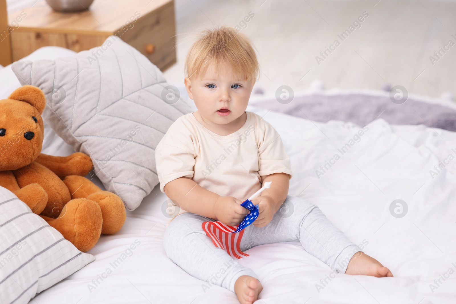 Photo of Cute little child with flag of USA on bed at home