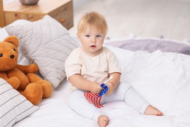 Photo of Cute little child with flag of USA on bed at home