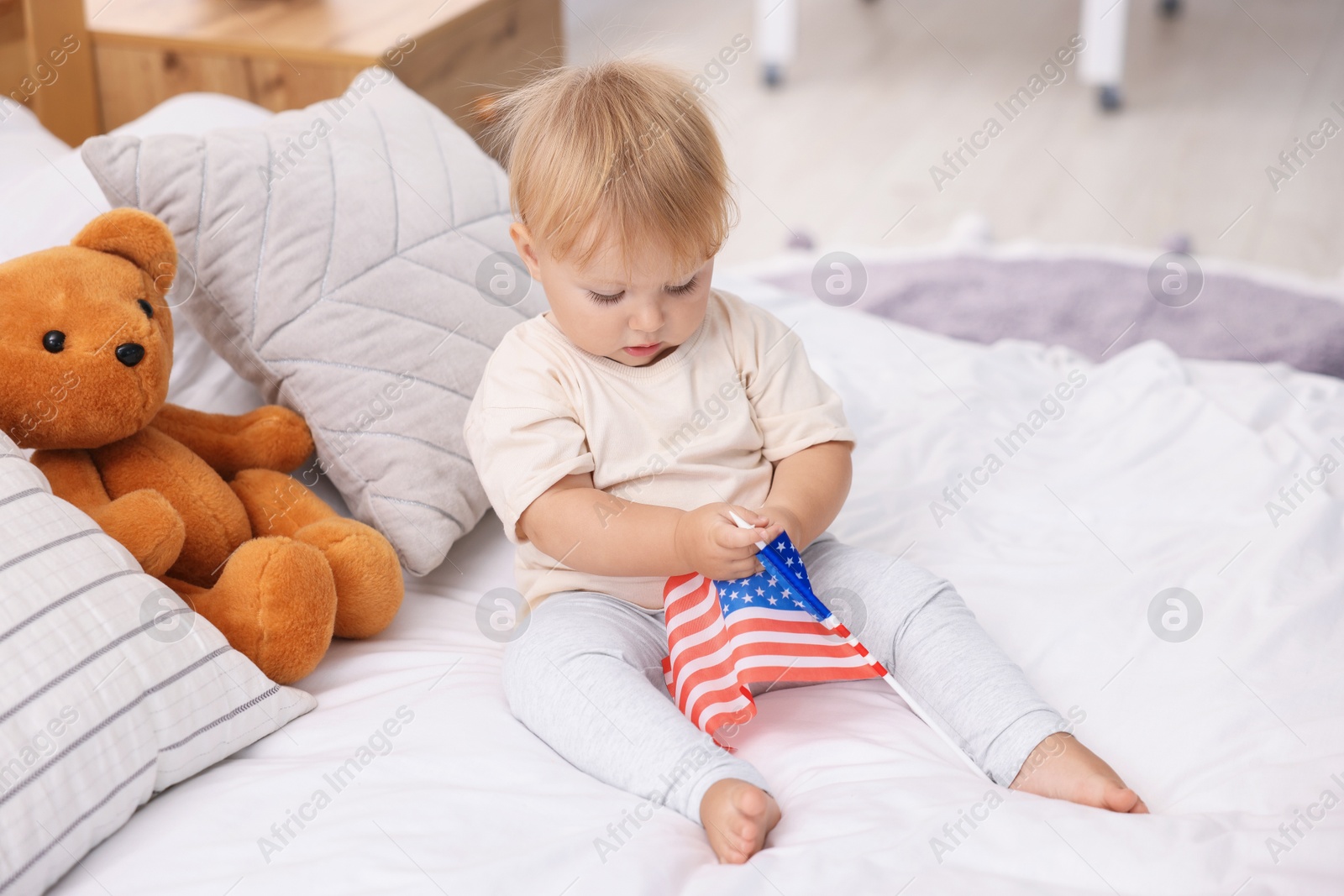 Photo of Cute little child with flag of USA on bed at home