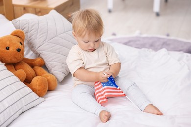 Photo of Cute little child with flag of USA on bed at home