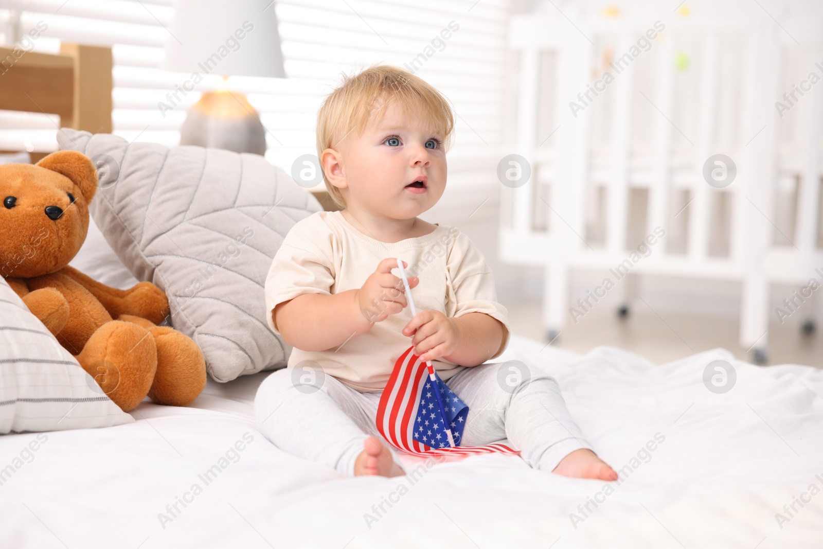 Photo of Cute little child with flag of USA on bed at home