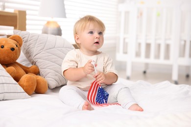 Photo of Cute little child with flag of USA on bed at home