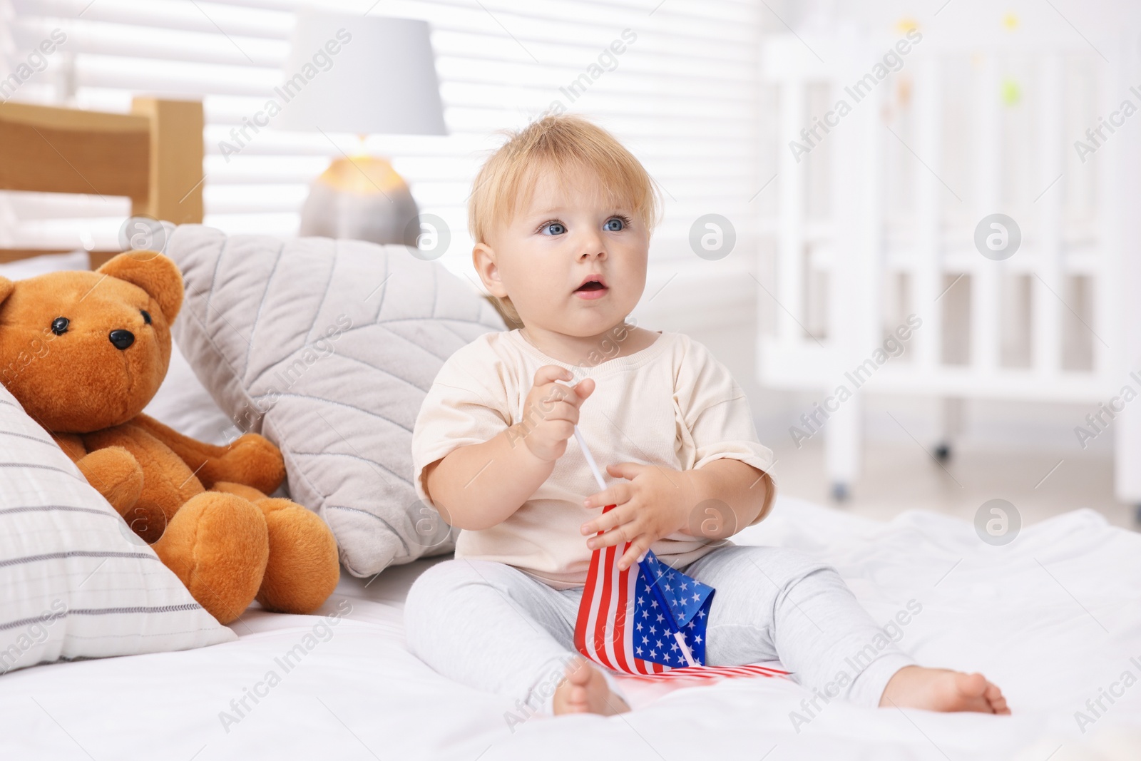Photo of Cute little child with flag of USA on bed at home