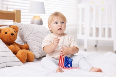 Photo of Cute little child with flag of USA on bed at home