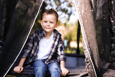 Photo of Cute little boy sitting on black trampoline outdoors