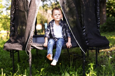 Photo of Cute little boy sitting on black trampoline outdoors