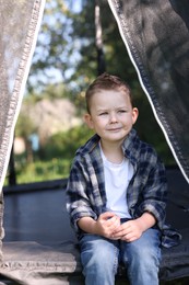 Photo of Cute little boy sitting on black trampoline outdoors