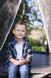 Photo of Happy little boy sitting on black trampoline outdoors