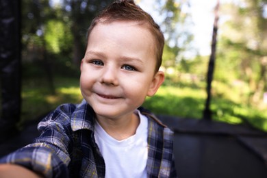 Photo of Cute little boy taking selfie on black trampoline outdoors
