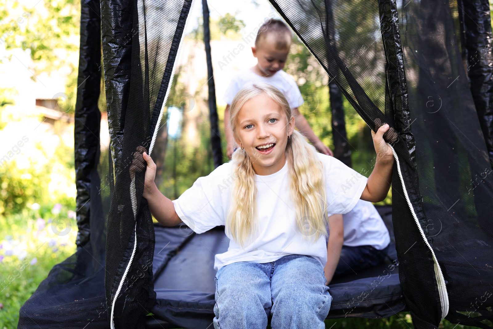 Happy little girl and her friends on black trampoline outdoors Photo of Happy little girl and her friends on black trampoline outdoors
