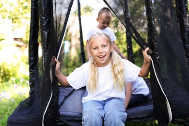 Photo of Happy little girl and her friends on black trampoline outdoors