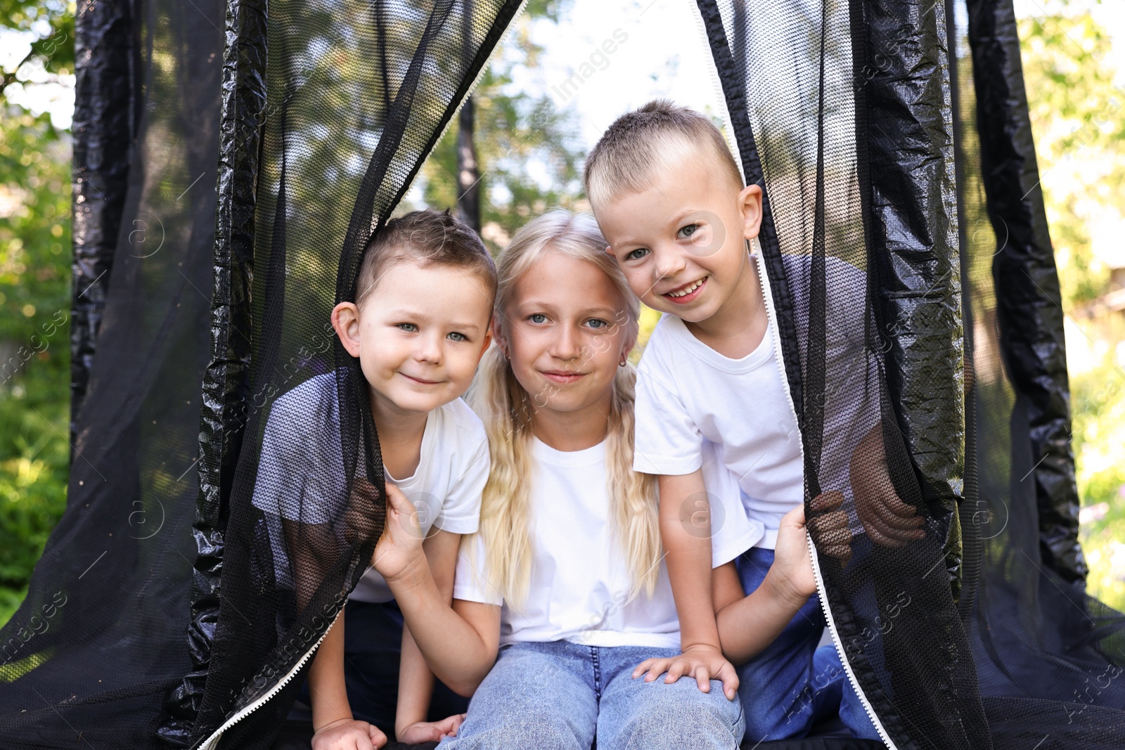 Happy children posing on black trampoline outdoors Photo of Happy children posing on black trampoline outdoors