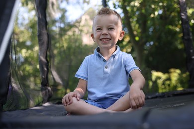 Photo of Happy little boy sitting on black trampoline outdoors