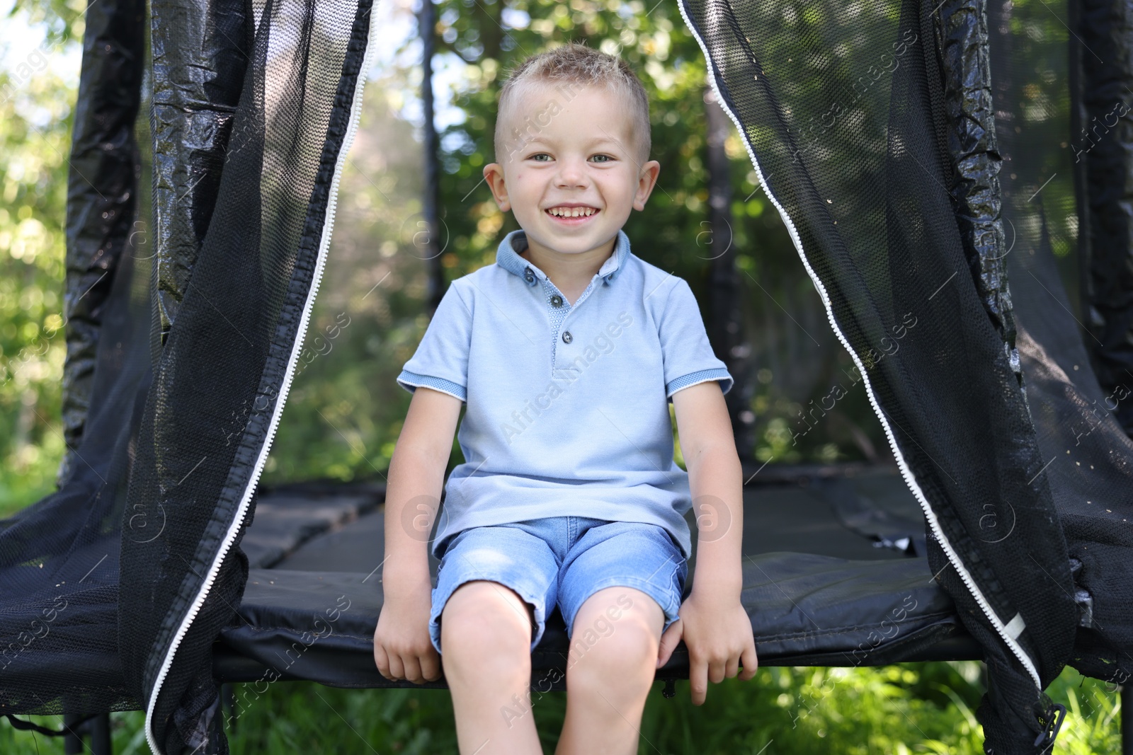 Happy little boy sitting on black trampoline outdoors Photo of Happy little boy sitting on black trampoline outdoors