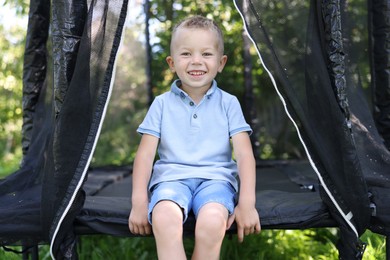 Photo of Happy little boy sitting on black trampoline outdoors