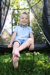 Photo of Happy little boy sitting on black trampoline outdoors, low angle view