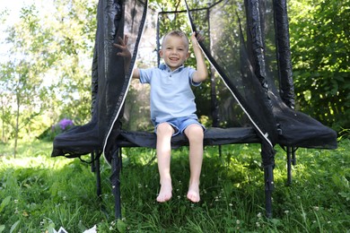 Photo of Happy little boy sitting on black trampoline outdoors