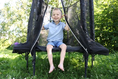 Photo of Happy little boy sitting on black trampoline outdoors