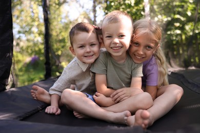 Photo of Happy little friends posing on black trampoline outdoors