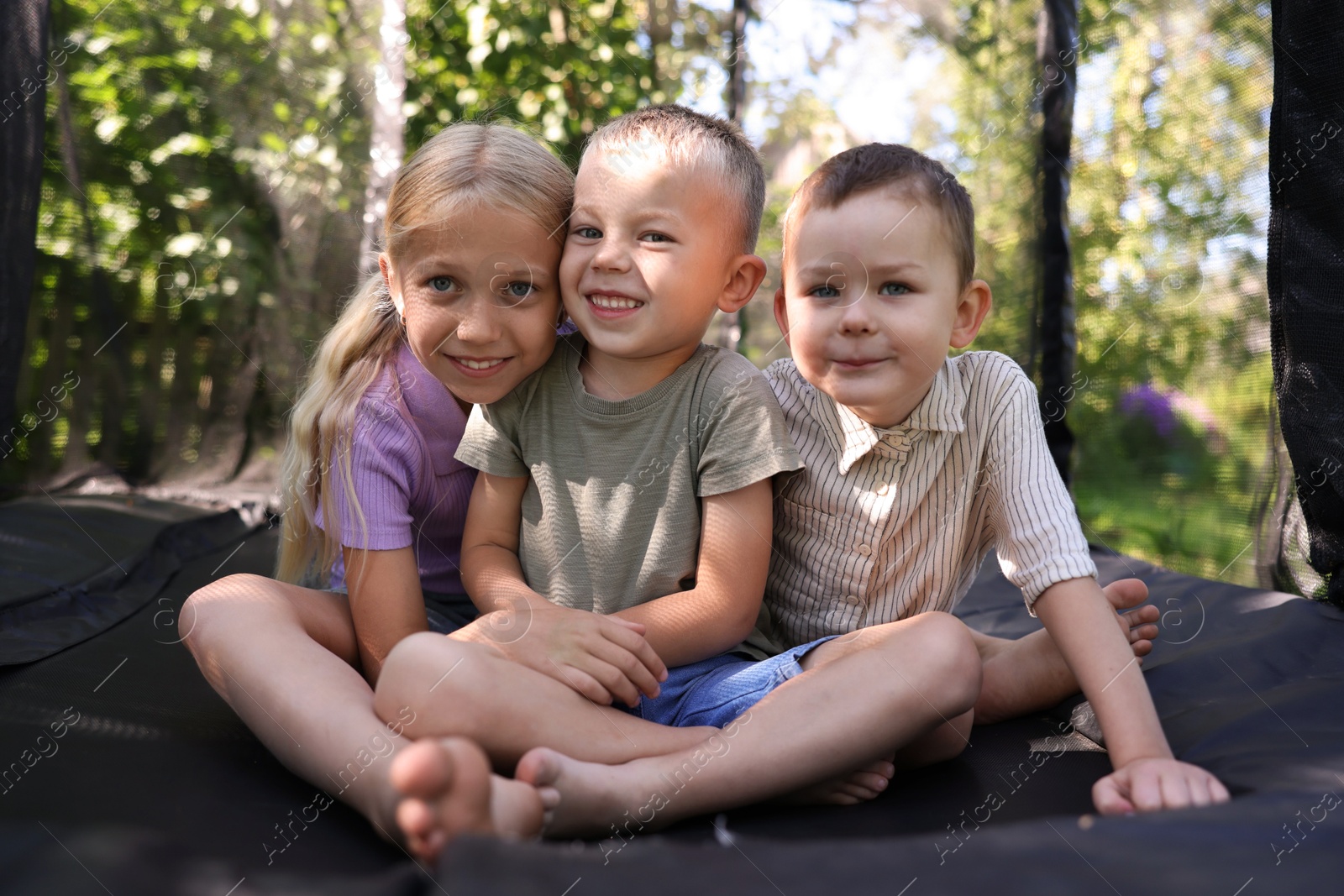 Happy little friends posing on black trampoline outdoors Photo of Happy little friends posing on black trampoline outdoors