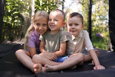 Photo of Happy little friends posing on black trampoline outdoors