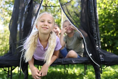 Photo of Happy little girl and her friends having fun on black trampoline outdoors